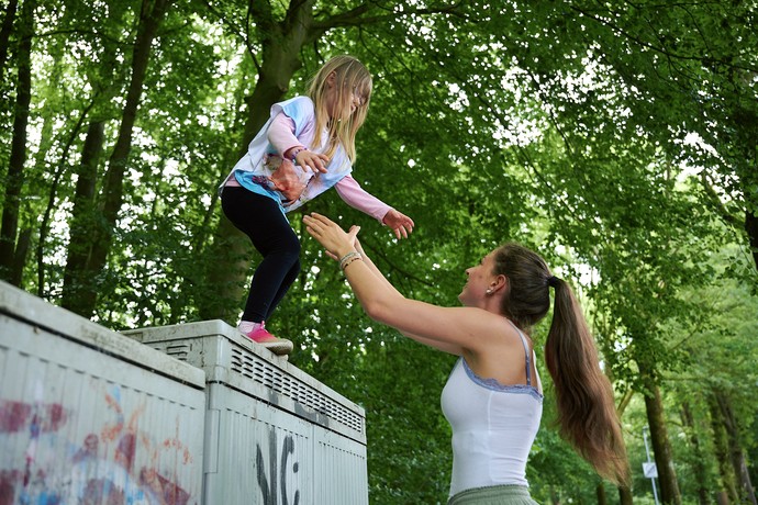 Eine junge Frau hilft einem Kind beim Springen von einem Kasten.