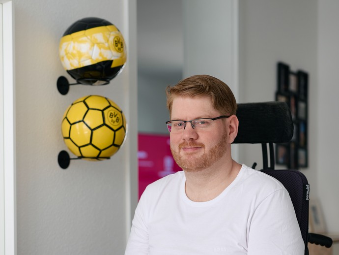 Neben Marcel W. liegen BVB-Fußballbälle auf einem Wandregal