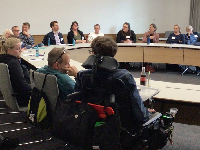 Teilnehmende im Workshopraum an einem runden Tisch (vergrößerte Bildansicht wird geöffnet)