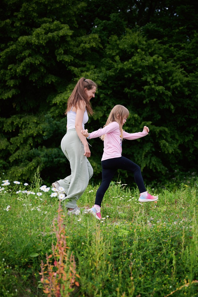 Eine junge Frau hüpft mit einem Kind über eine Wiese