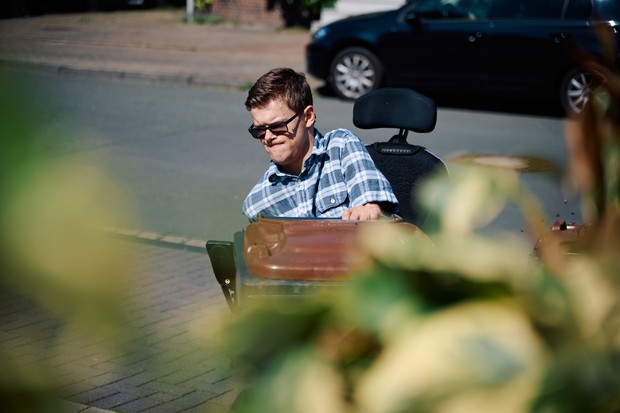Ein junger Mann, der einen Rollstuhl nutzt, bringt eine Mülltonne an die Straße