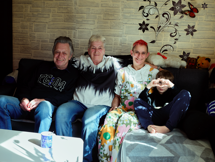 Eine Familie sitzt entspannt gemeinsam auf dem Sofa (vergrößerte Bildansicht wird geöffnet)